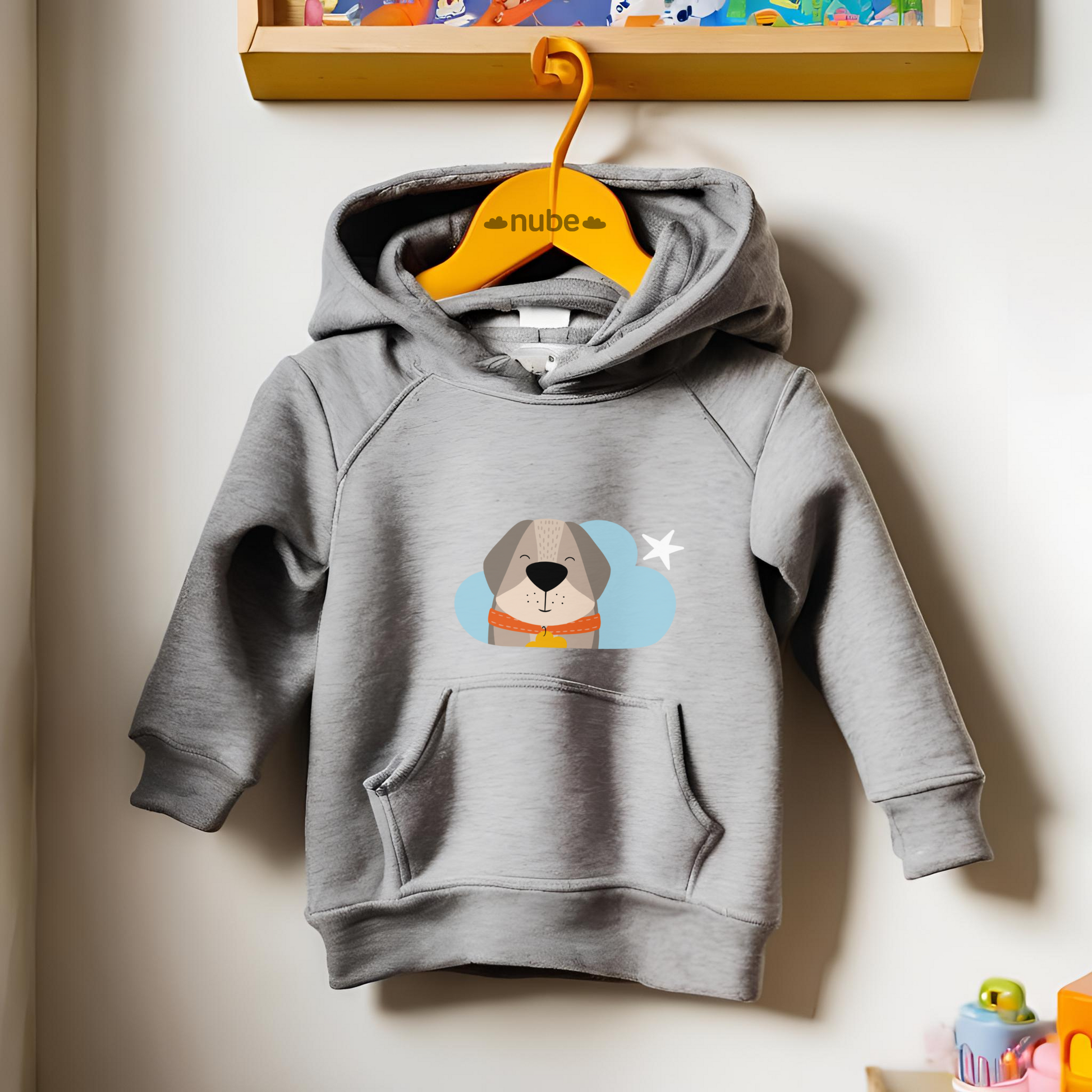 Sudadera tipo hoodie gris  colgada en un gancho con diseño de Leandro el Perro de la marca de ropa Nube con collar naranja y placa amarilla en forma de nube dentro de una nube azul y una estrella blanca a lado.