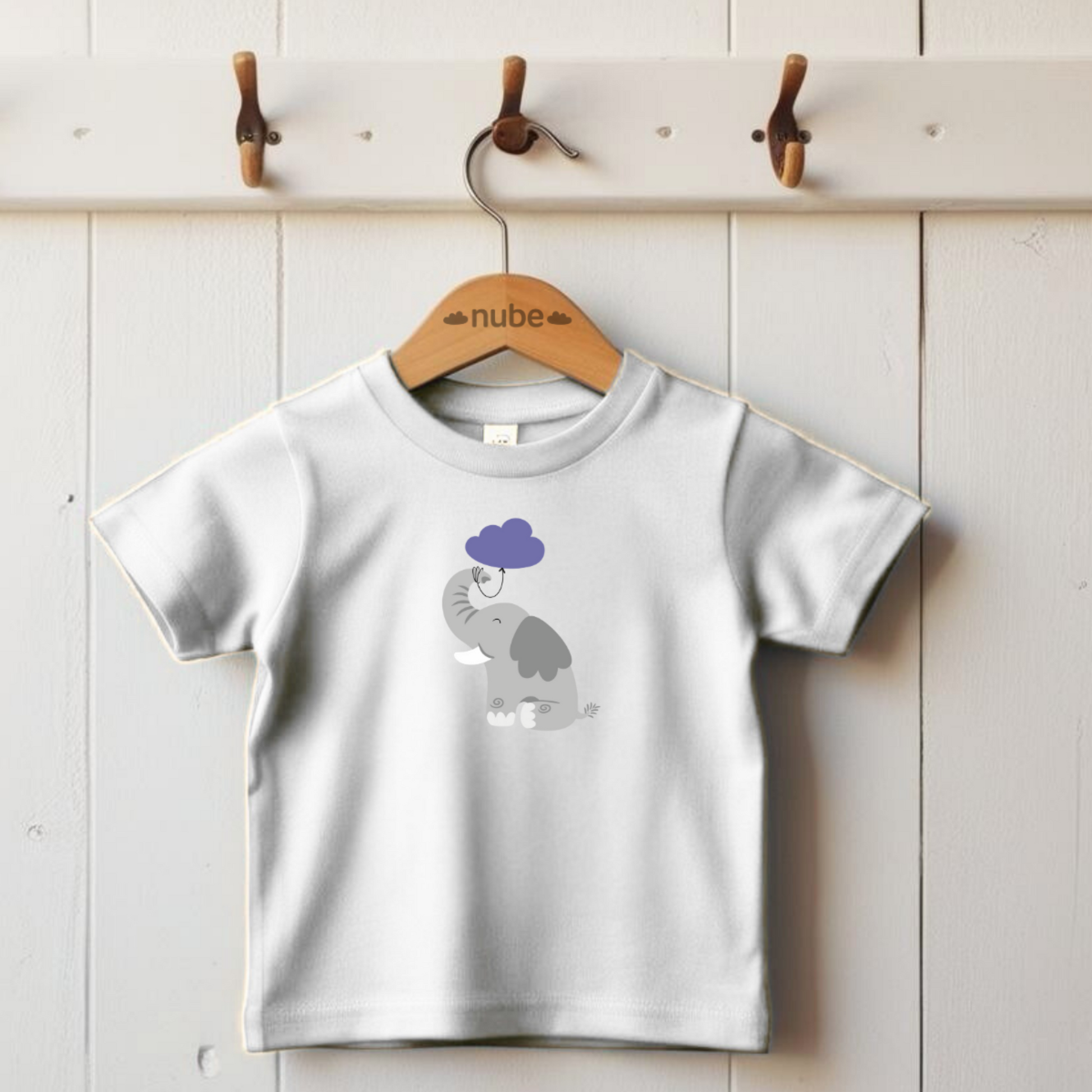 Playera blanca colgada de un gancho con diseño del elefante Clementino de la marca nube de pie con globo de nube morada amarrado a su trompa.