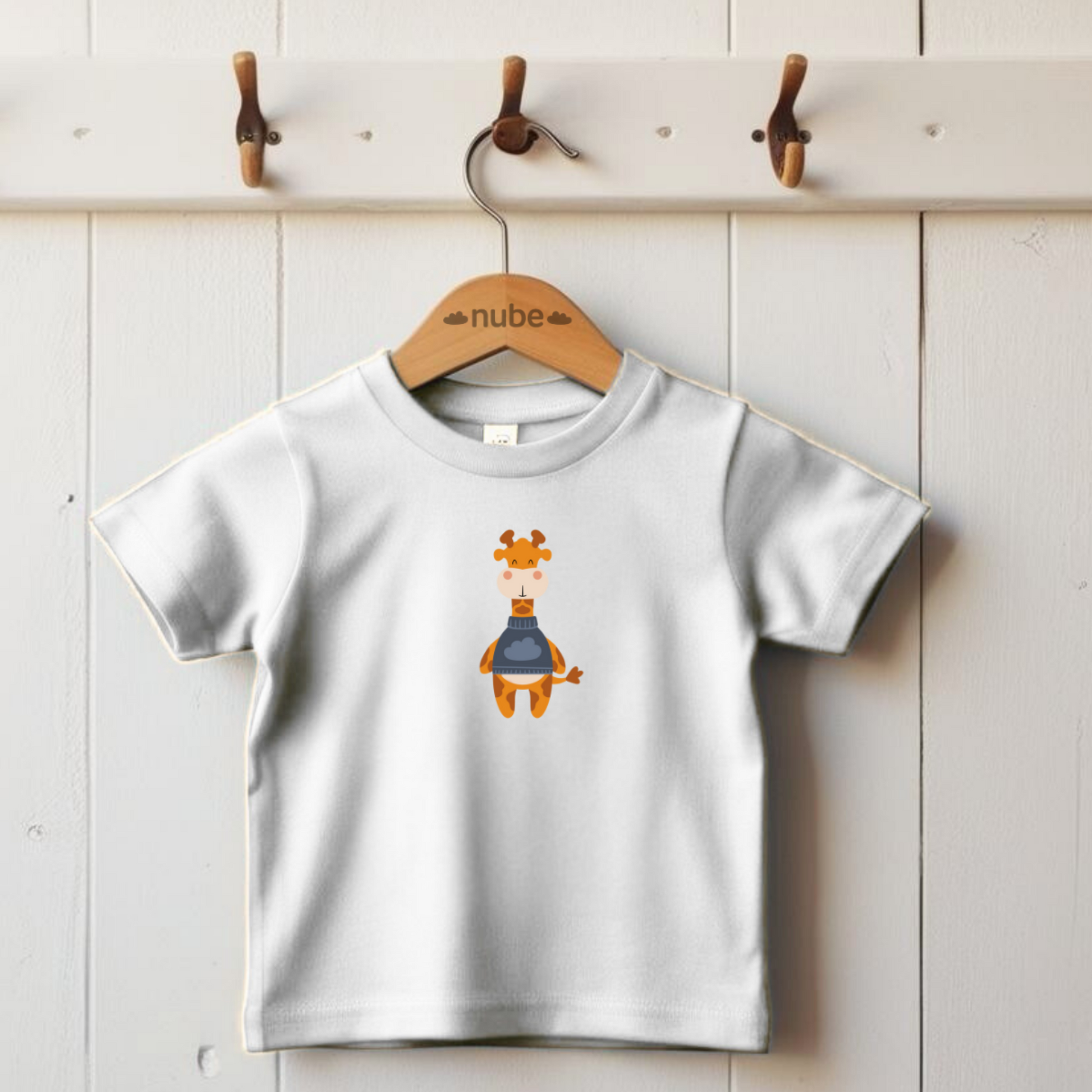 Playera blanca colgada en un gancho con diseño de la jirafa Lazaro de la marca nube de pie con sweater azul y dibujo de nube