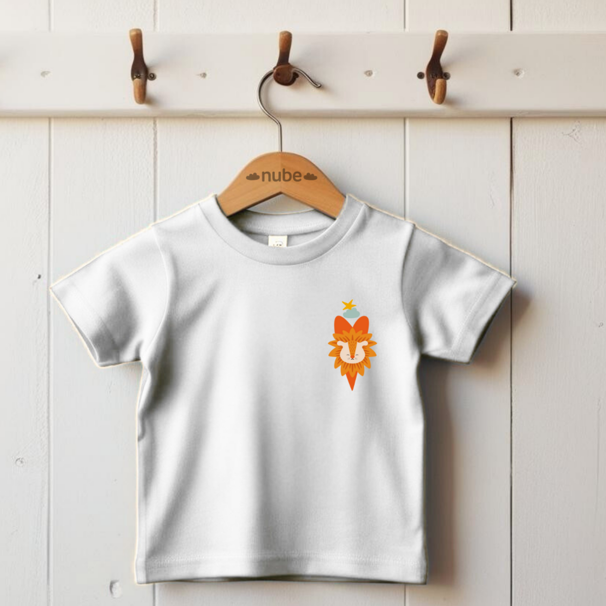Playera blanca colgada en un gancho con diseño del león  de la marca de ropa Nube dentro de un corazón naranja, nube azul y una estrella amarilla en la parte superior del pecho.