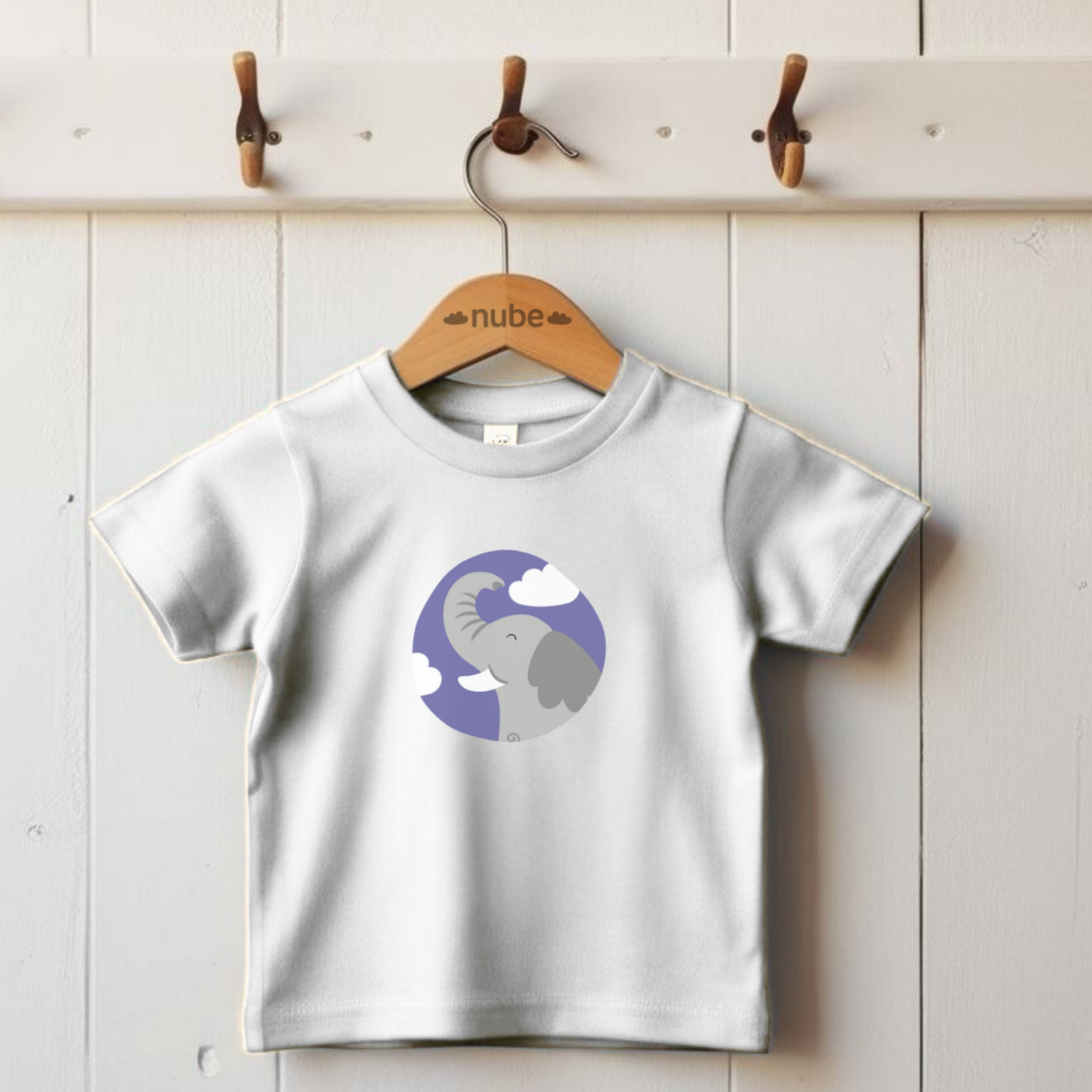 Playera blanca colgada en gancho con estampado del retrato del elefante Clementino de la marca de ropa Nube dentro de un círculo morado con nubes.