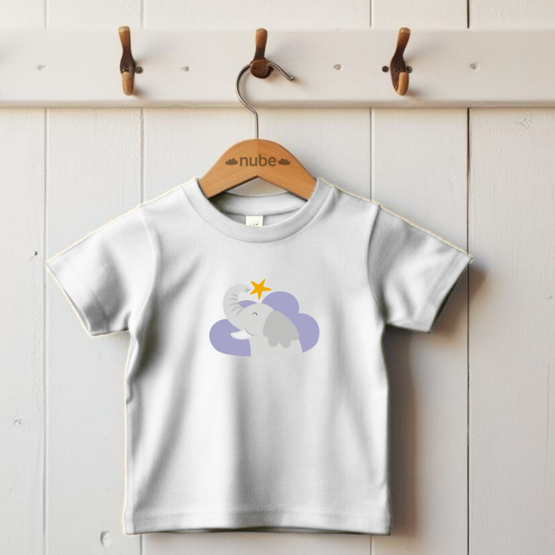 Playera blanca colgada en gancho con estampado del diseño del elefante clementino de la marca de ropa nube dentro de una nube morada. Arriba lo guía una estrella amarilla.