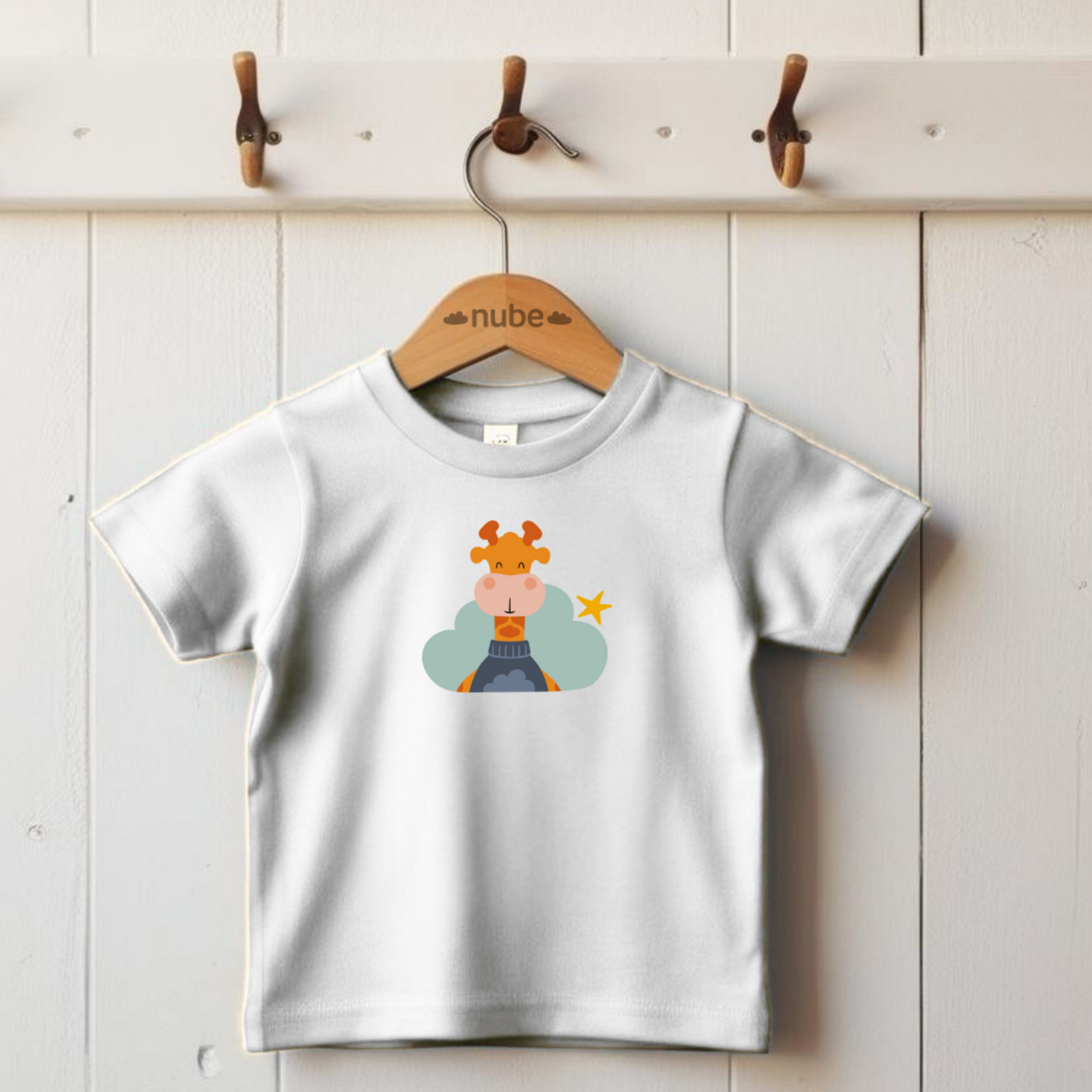 Playera blanca colgada en un gancho con estampado del diseño de la jirafa Lázaro de la marca Nube en una Nube color verde y una estrella amarilla