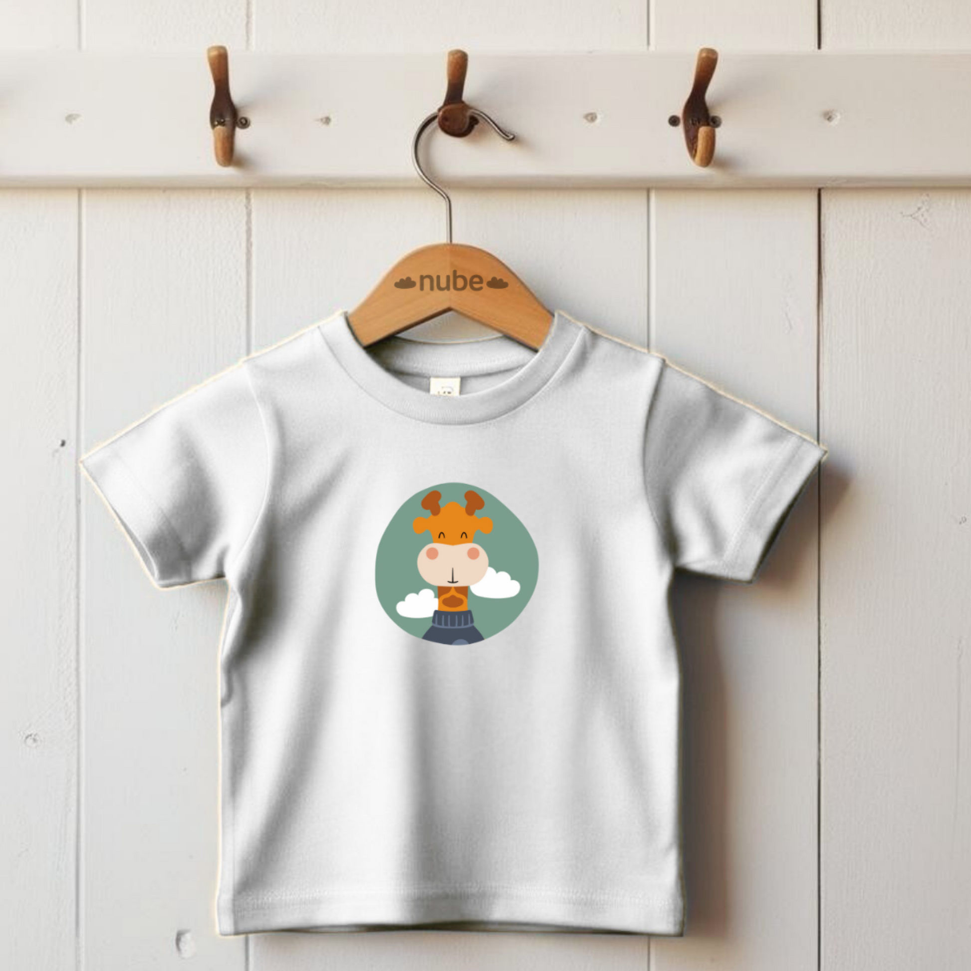 Playera blanca colgada en gancho con estampado del retrato de la jirafa Lazaro de la marca de ropa nube con un sweater azul dentro de un círculo verde con nubes.