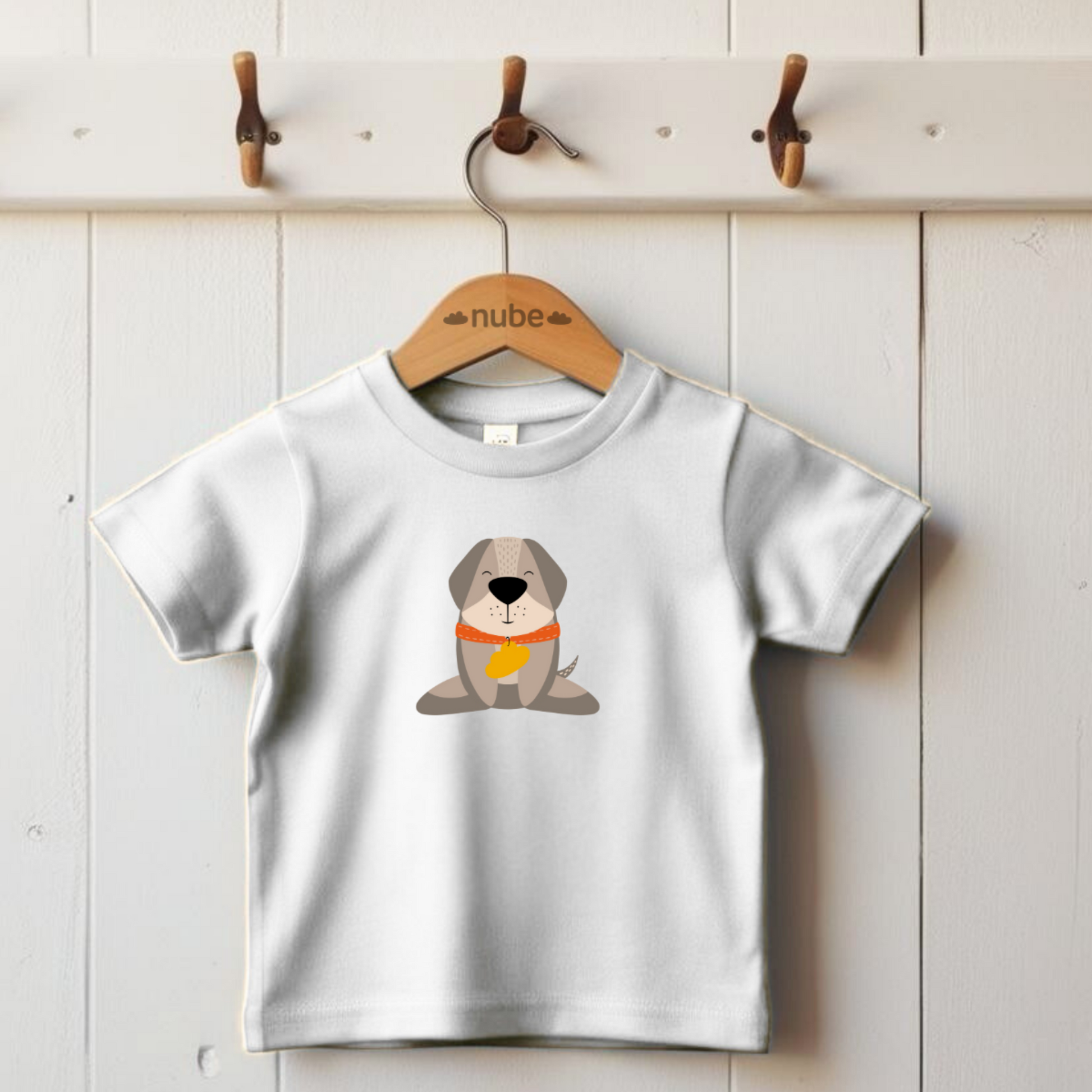 Playera blanca colgada en gancho con estampado del diseño del perro Leandro de pie con collar naranja y placa amarilla de la marca de ropa nube.