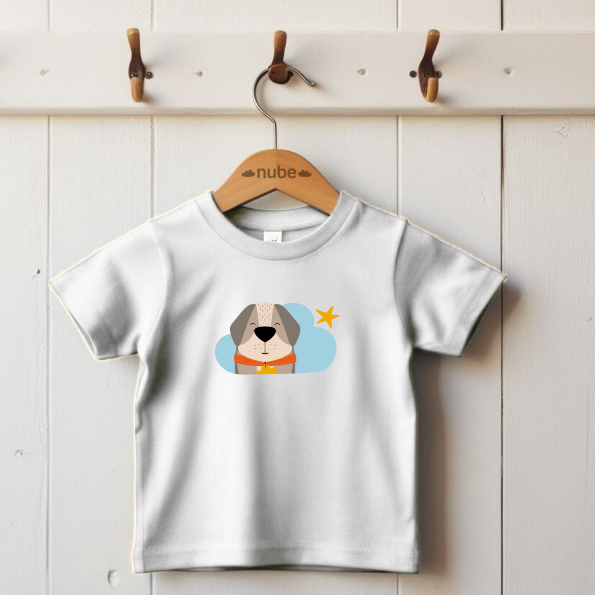 Playera blanca colgada en un gancho con estampado del diseño del perro Leandro de la marca de ropa nube con collar naranja y placa amarilla en una Nube color azul y una estrella amarilla