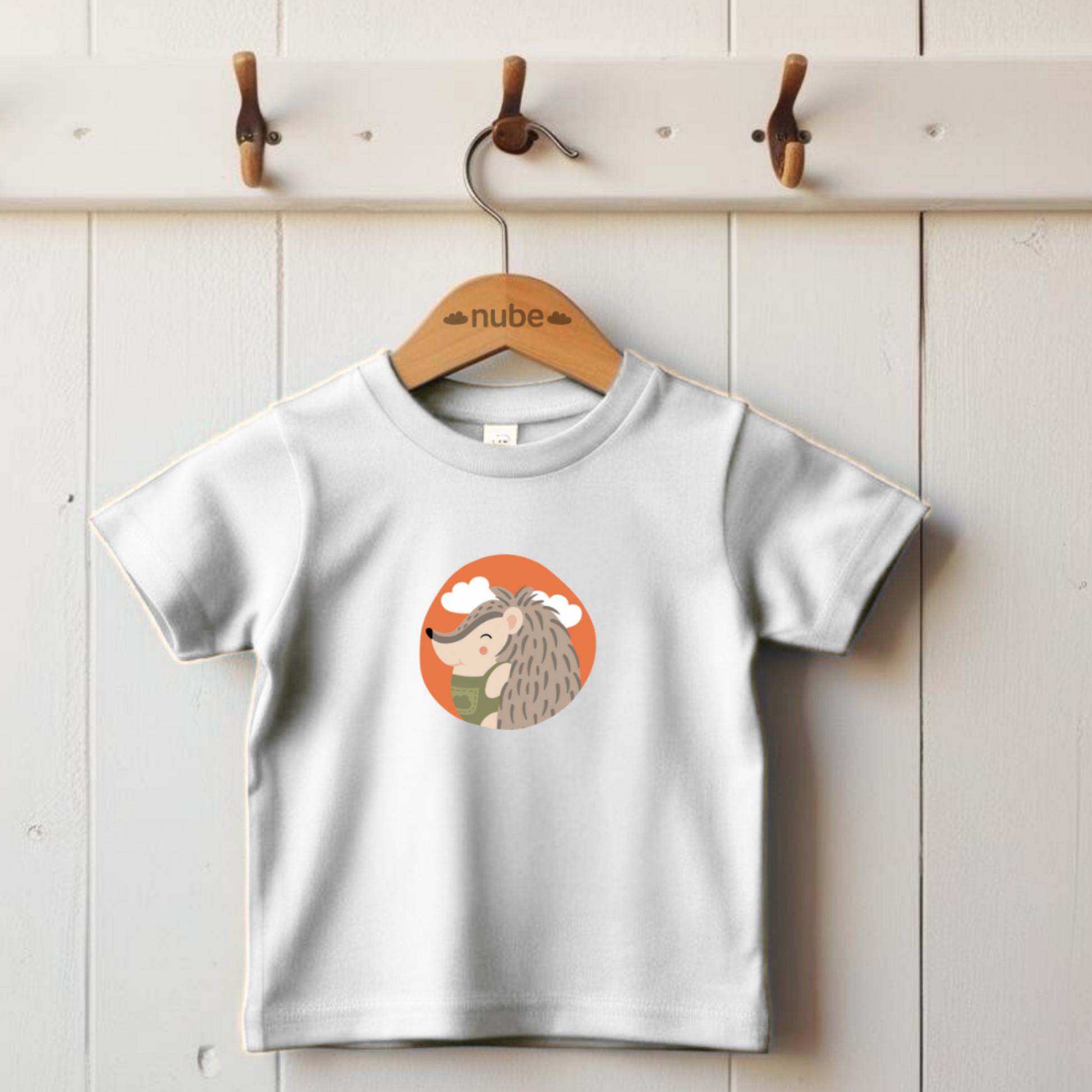 Playera blanca colgada en gancho con estampado del retrato del puercoespin Filomeno de la marca de ropa Nube con un traje verde dentro de un círculo naranja con nubes.