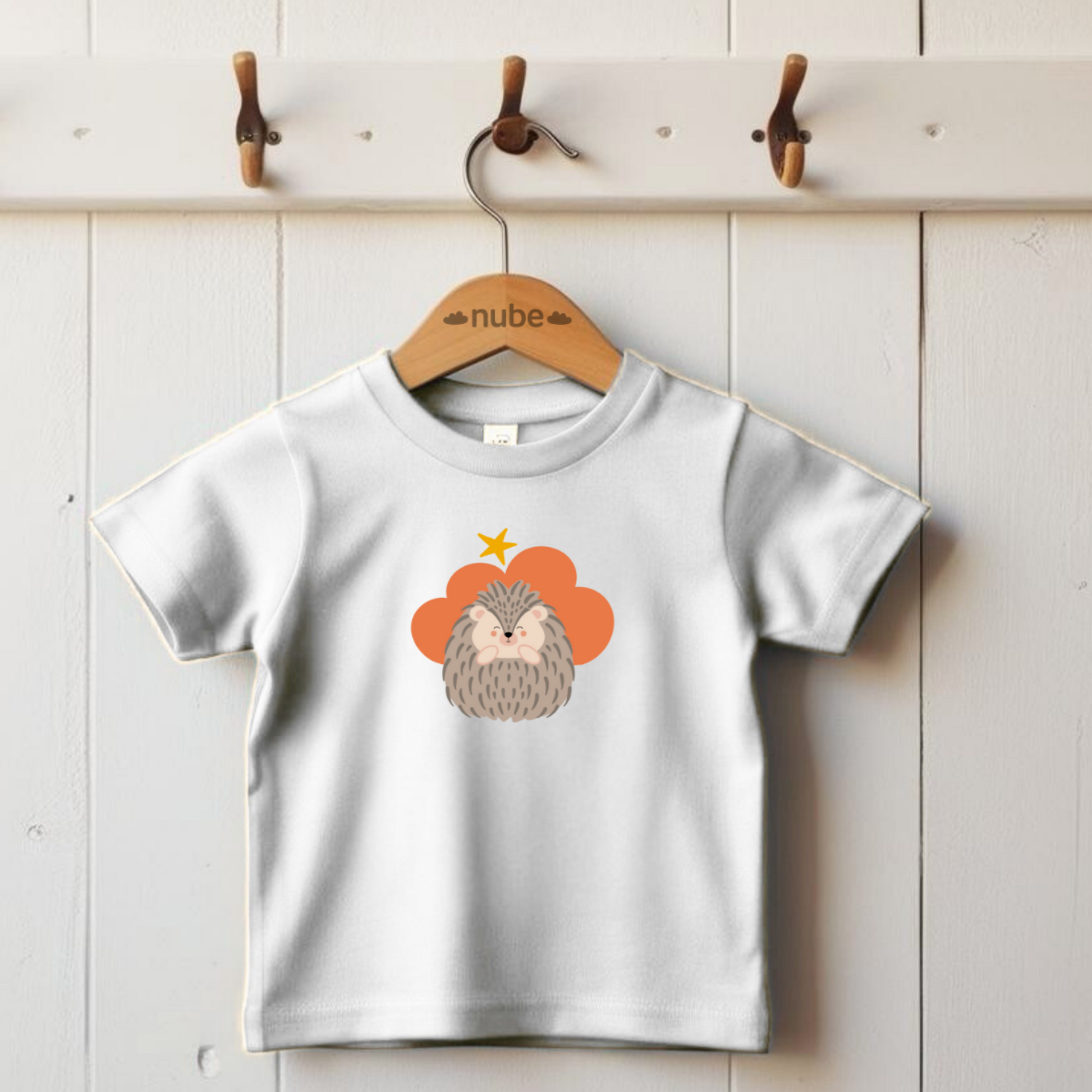 Playera blanca colgada en un gancho con estampado del diseño del puercoespin Filomeno de la marca Nube en una Nube color naranja y una estrella amarilla