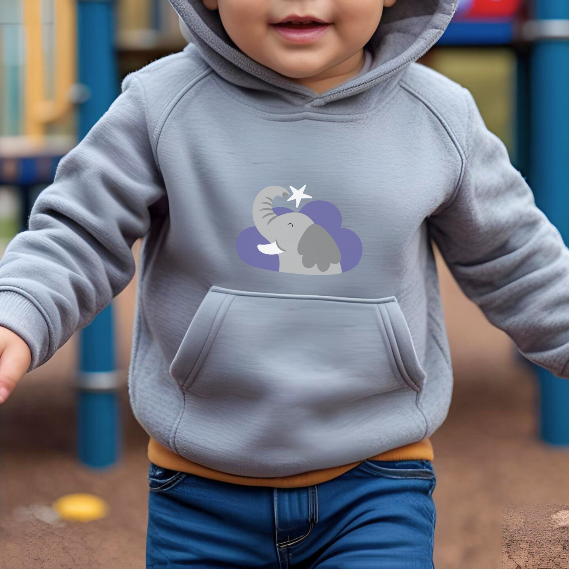 Toddler jugando en el parque con sudadera tipo hoodie gris con diseño de Clementina la Elefanta de la marca de ropa Nube dentro de una nube morada y una estrella blanca a lado.