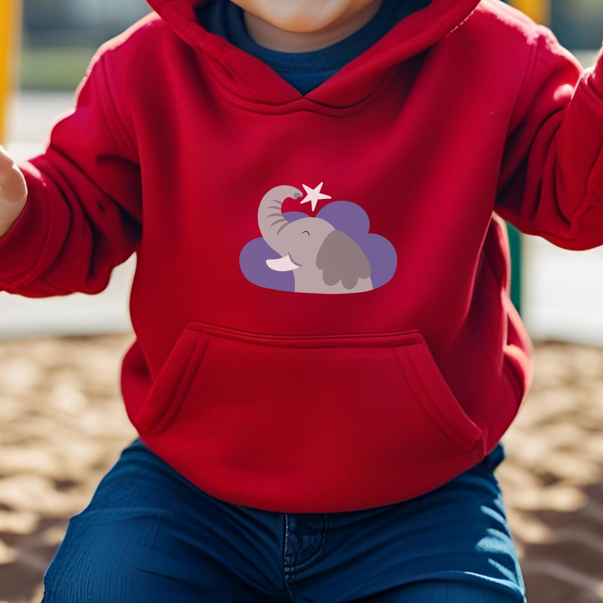 Toddler jugando en el parque con sudadera tipo hoodie rojo con diseño de Clementina la Elefanta de la marca de ropa Nube dentro de una nube morada y una estrella blanca a lado.