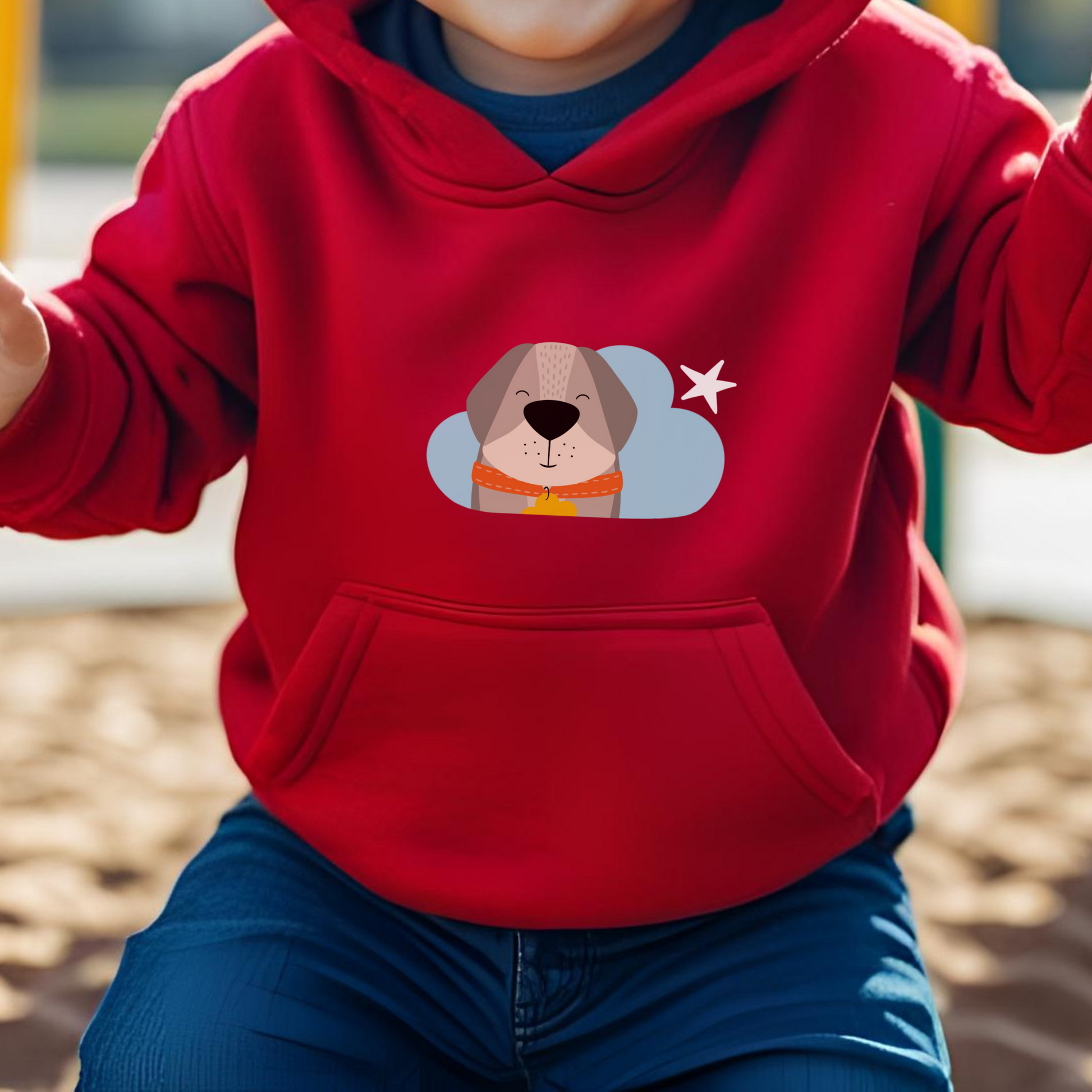 Toddler jugando en el parque con sudadera tipo hoodie roja con diseño de Leandro el Perro de la marca de ropa Nube con collar naranja y placa amarilla en forma de nube dentro de una nube azul y una estrella amarilla a lado.
