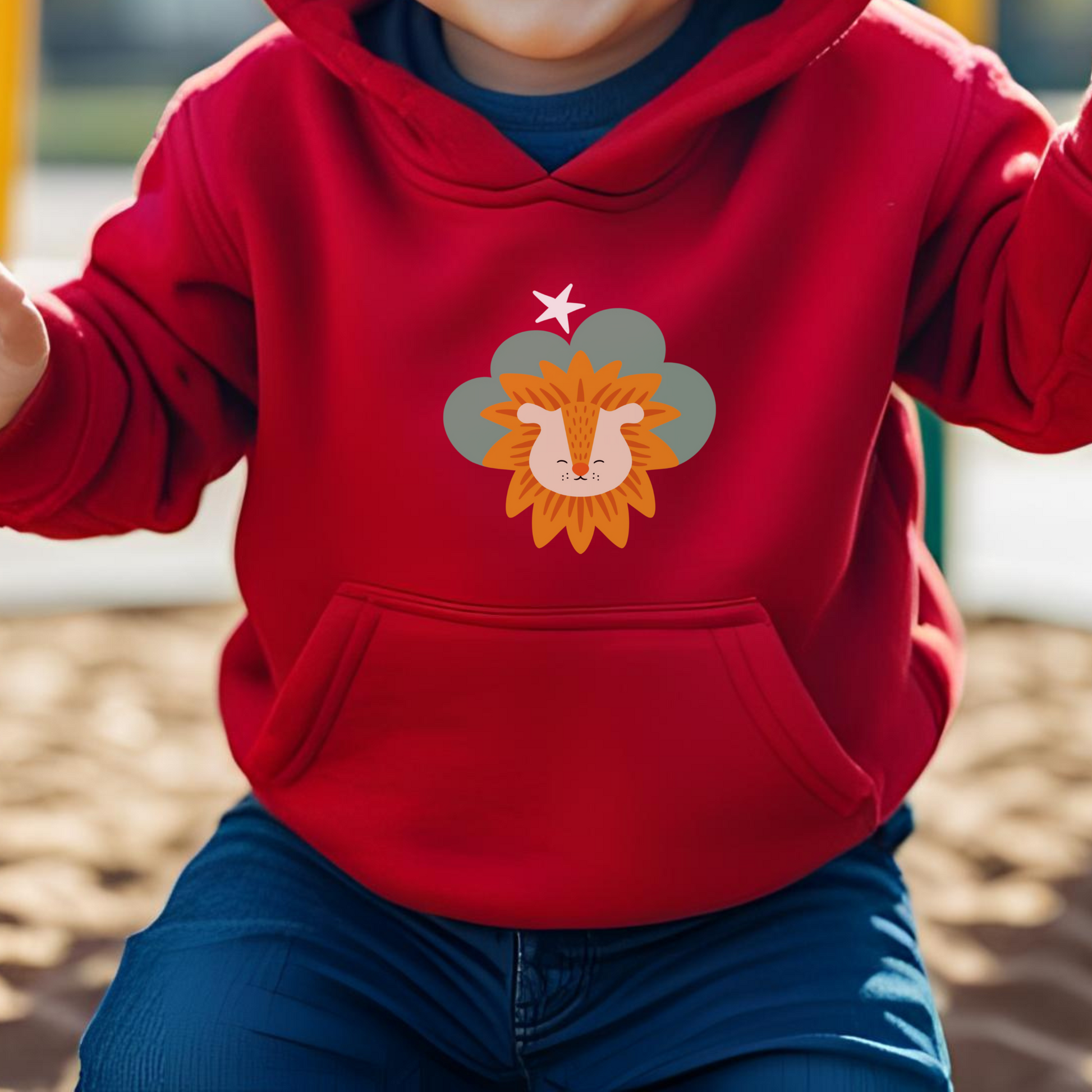 Toddler jugando en el parque con sudadera tipo hoodie roja con diseño de Sabino el León de la marca de ropa Nube dentro de una nube verde y una estrella blanca a lado.