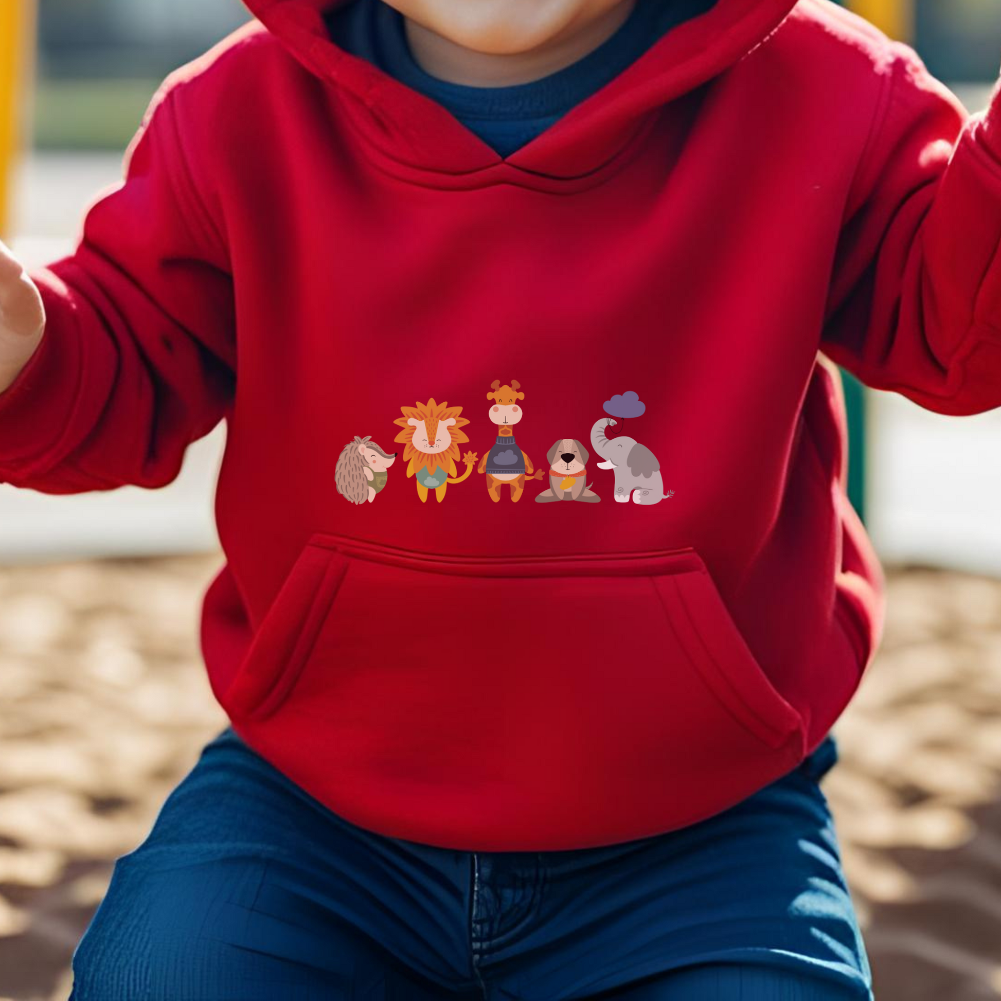 Toddler jugando en el parque con sudadera tipo hoodie roja con diseño de la manada  de la marca de ropa Nube: Filomena el puercoespín, Sabino el león, Lázaro la jirafa, Leandro el perro y Clementina la elefanta.