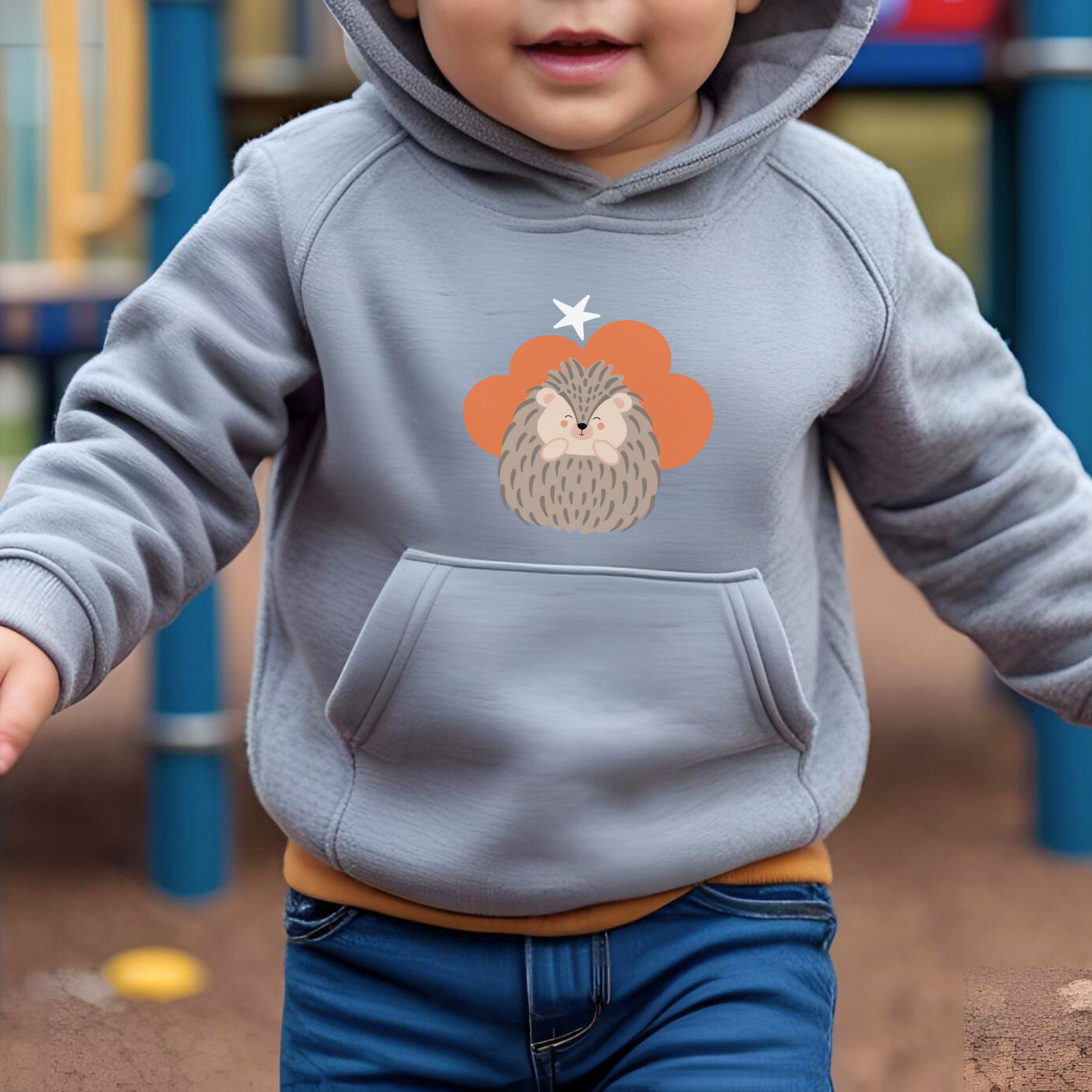 Toddler jugando en el parque con sudadera tipo hoodie gris con diseño de Filomena el Puercoespín de la marca de ropa Nube dentro de una nube naranja y una estrella blanca a lado.