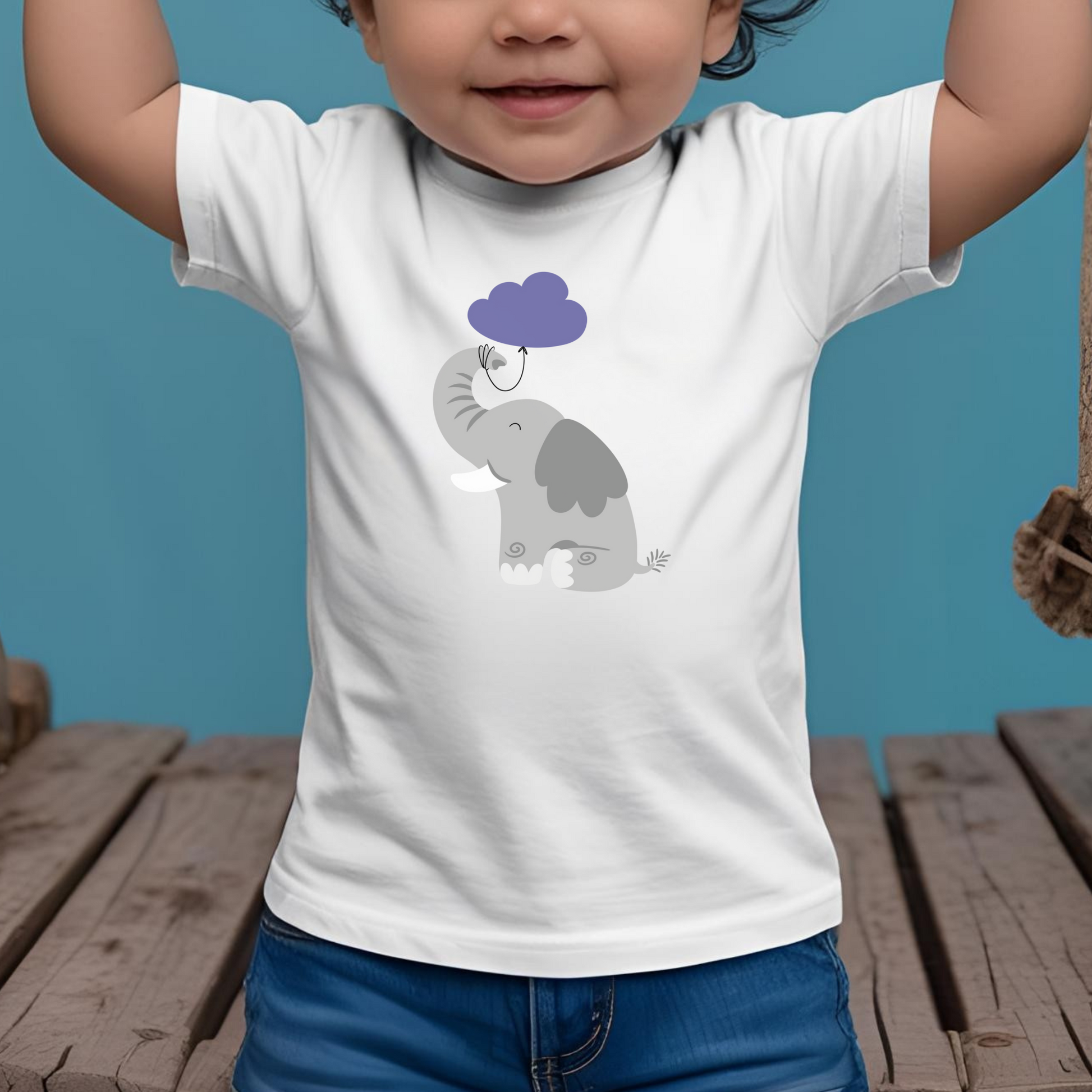 Toddler sentado en puente de madera con playera blanca con diseño de un elefante gris con globo de nube morada amarrada a su trompa
