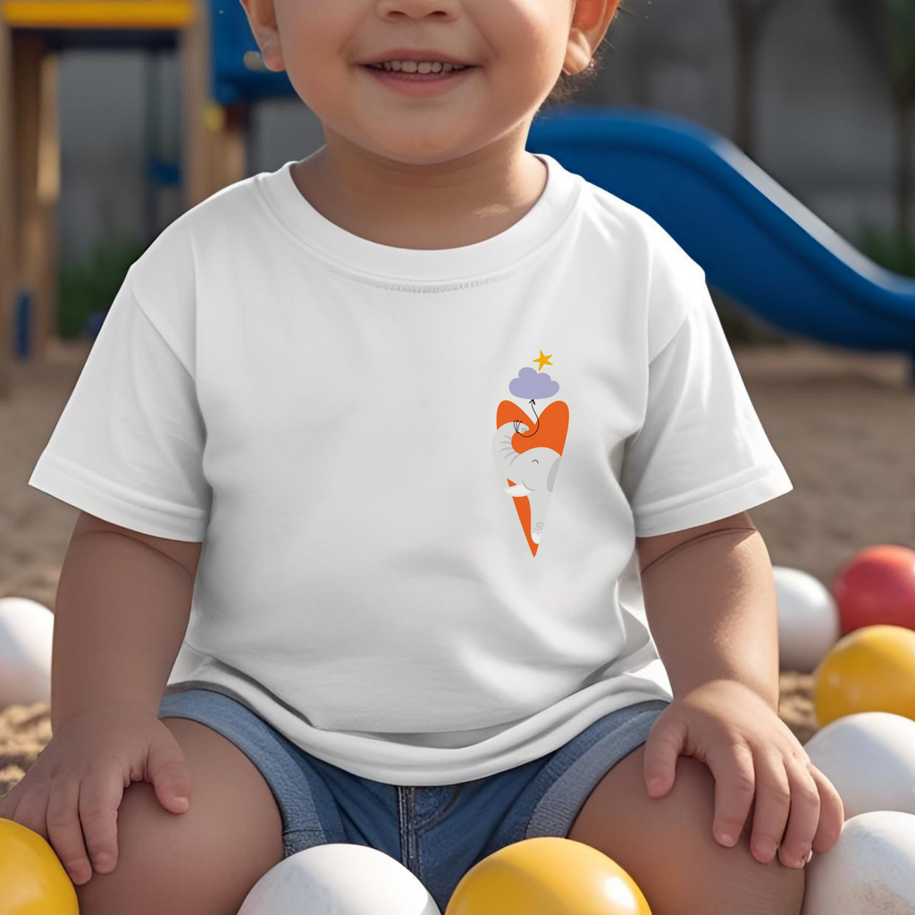 Toddler jugando en el parque con playera blanca con diseño de un elefante gris dentro de un corazón naranja, con globo de nube morada amarrada a su trompa y una estrella amarilla en la parte superior lo guía.