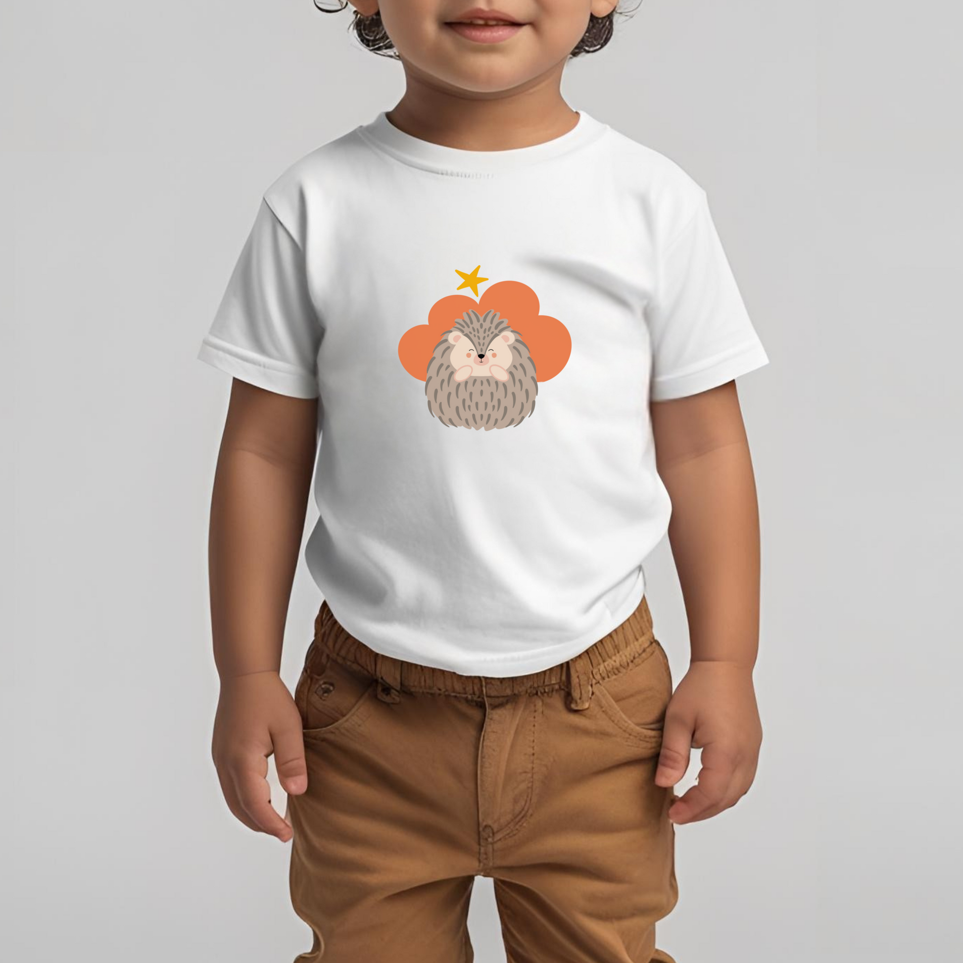 Toddler con pantalones cafés y playera blanca de la marca de ropa nube con estampado del puercoespín Filomeno dentro de un corazón naranja. Arriba lo guía una estrella amarilla.