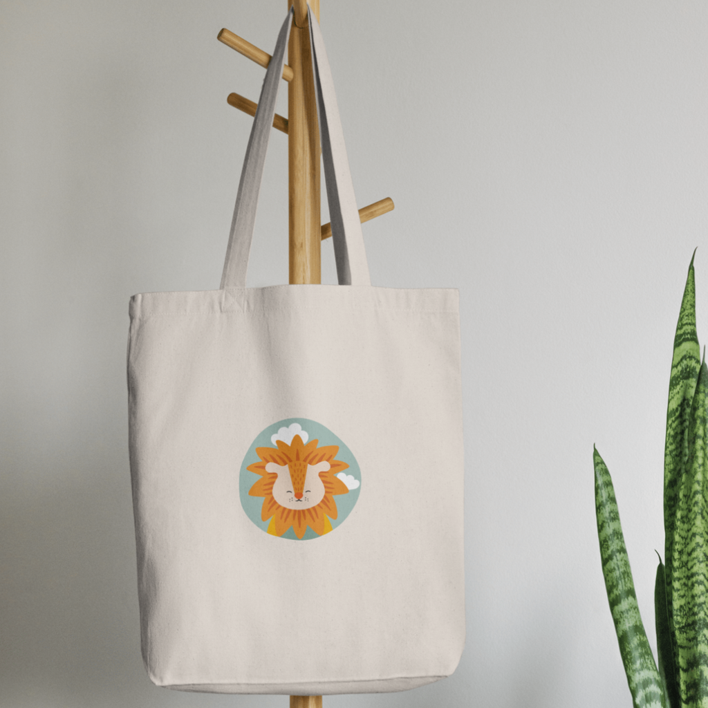 Bolsa Tote Bag color beige en  perchero, mostrando el retrato del leon Sabino de la marca de ropa nube dentro de un círculo verde con nubes.