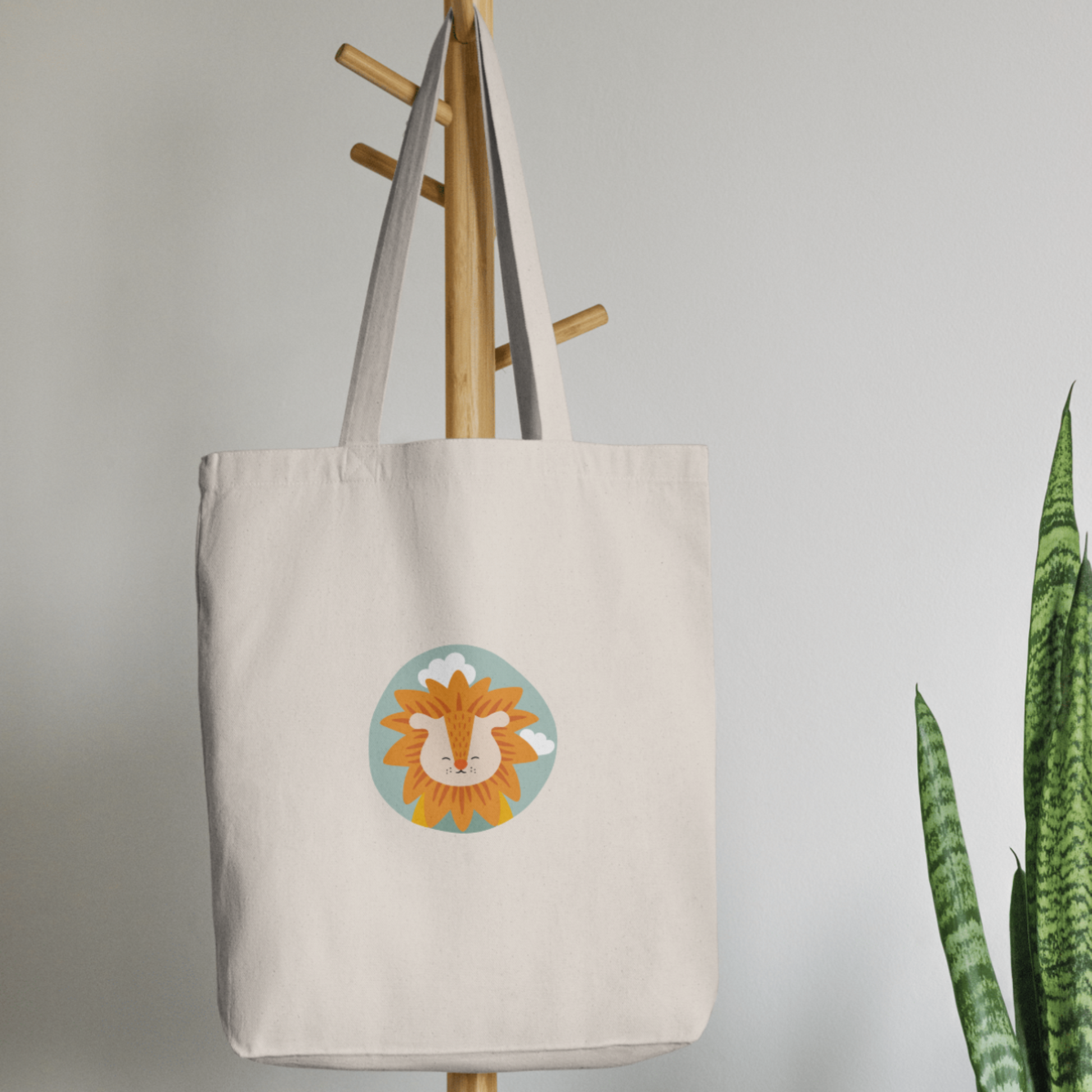 Bolsa Tote Bag color beige en  perchero, mostrando el retrato del leon Sabino de la marca de ropa nube dentro de un círculo verde con nubes.