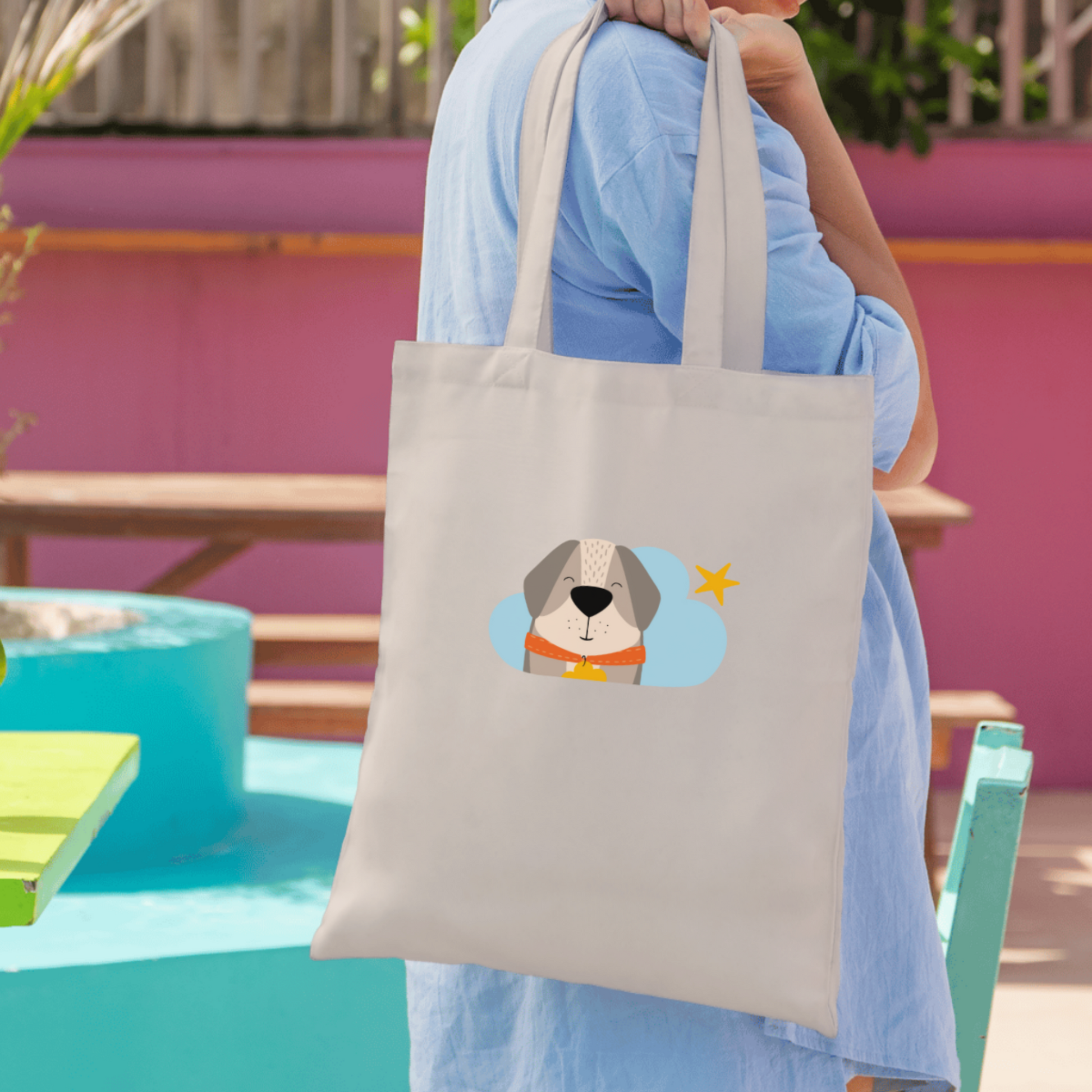 Mujer con camisa azul sostiene la bolsa tote bag de la marca de ropa nube con estampado del perro Leandro en una Nube color azul y una estrella amarilla