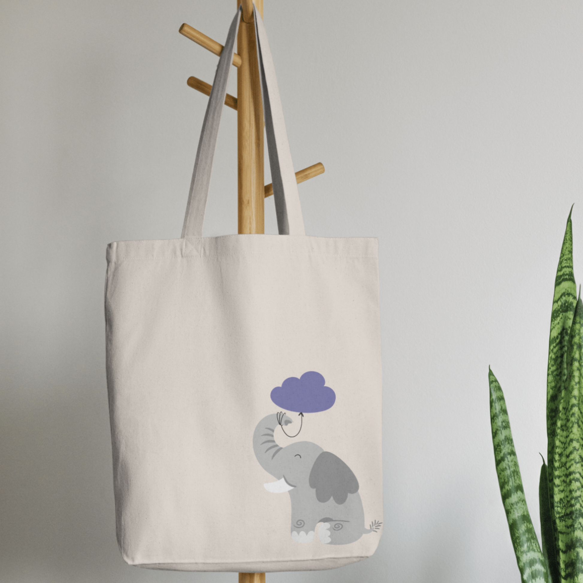 Bolsa Tote Bag color beige en  perchero, mostrando el estampado del elefante Clementino con un globo morado de nube amarrado desde su trompa