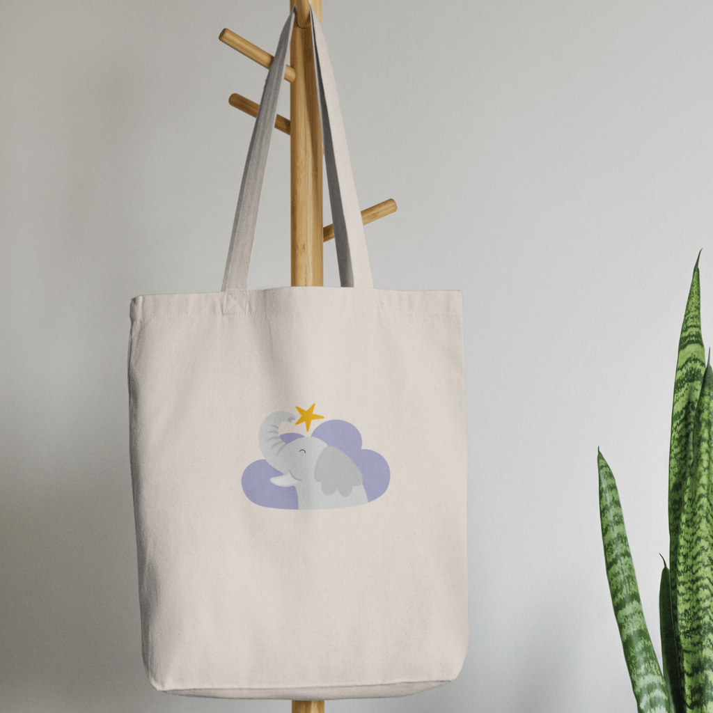 Bolsa Tote Bag color beige en  perchero, mostrando el estampado del elefante Clementino en una nube morada y una estrella amarilla