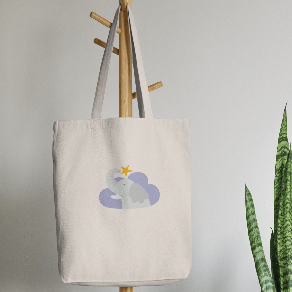 Bolsa Tote Bag color beige en  perchero, mostrando el estampado del elefante Clementino en una nube morada y una estrella amarilla