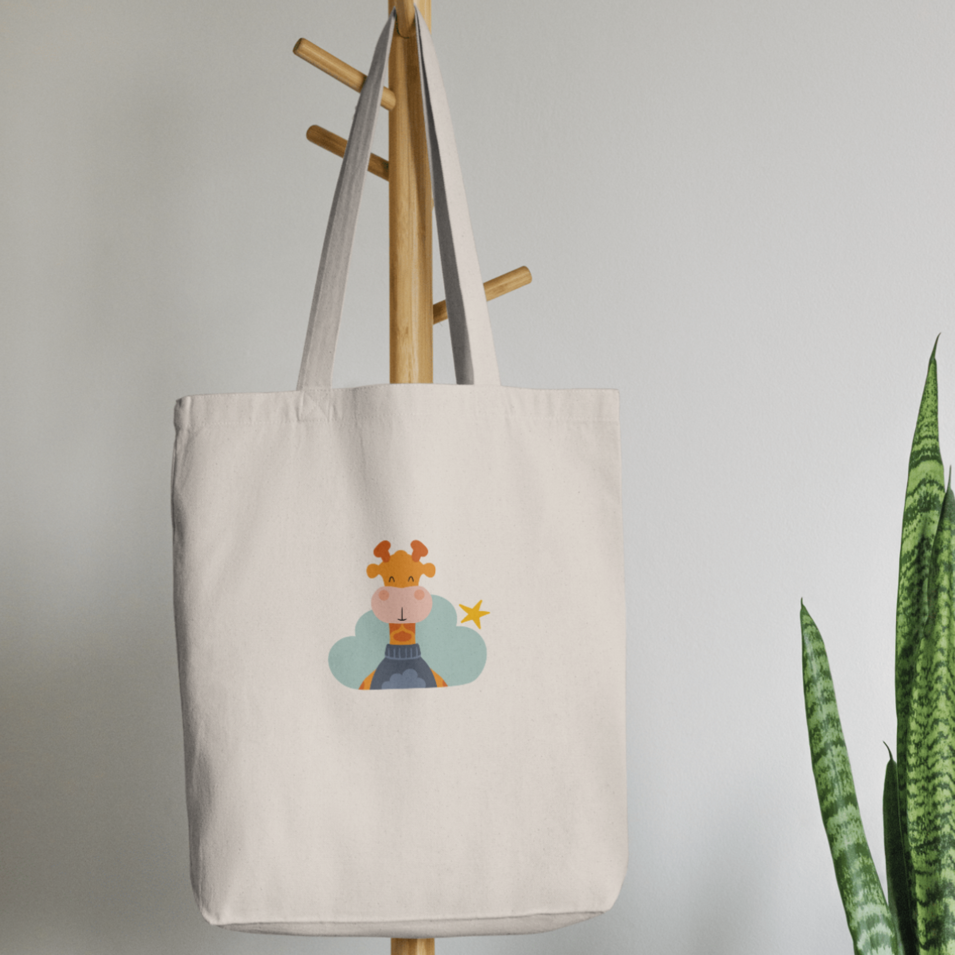 Bolsa Tote Bag color beige en  perchero, mostrando el estampado de la jirafa Lazaro en una Nube color verde y una estrella amarilla