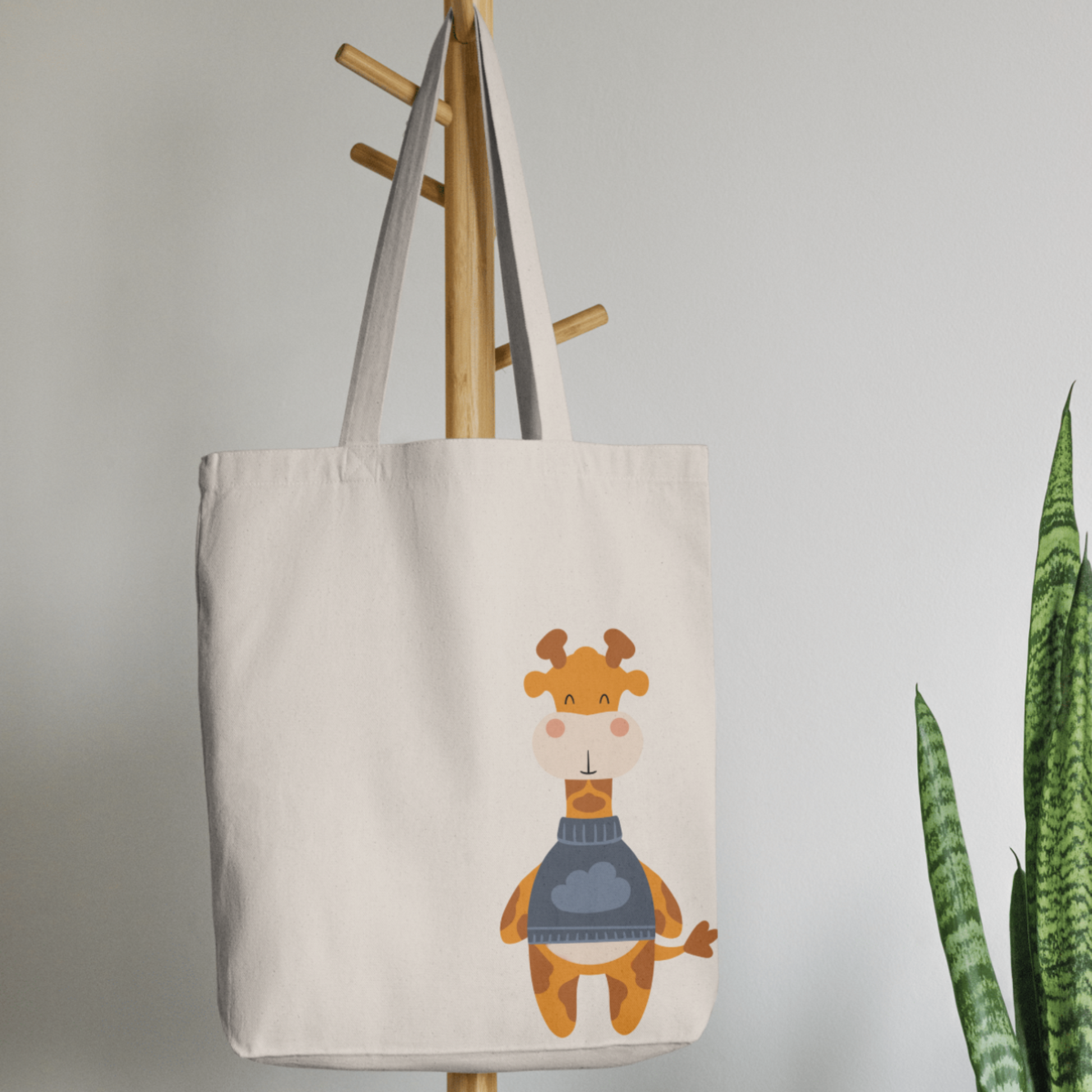 Bolsa Tote Bag color beige en  perchero, mostrando el estampado de la jirafa Lazaro León con sweater azul y dibujo de nube