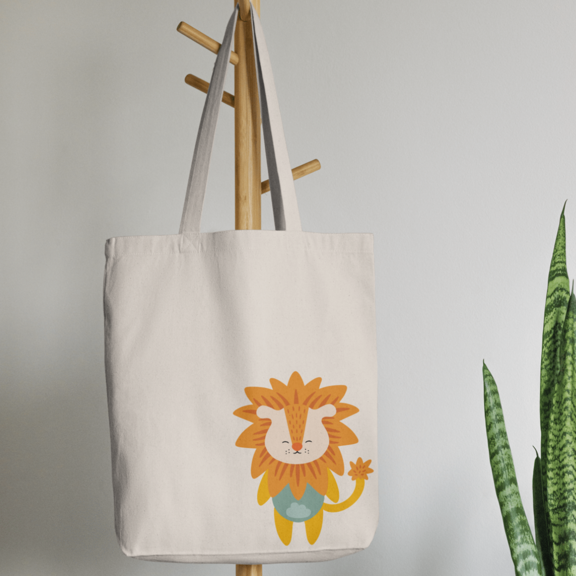 Bolsa Tote Bag color beige en  perchero, mostrando el estampado del León Sabino de melena naranja y ropa verde