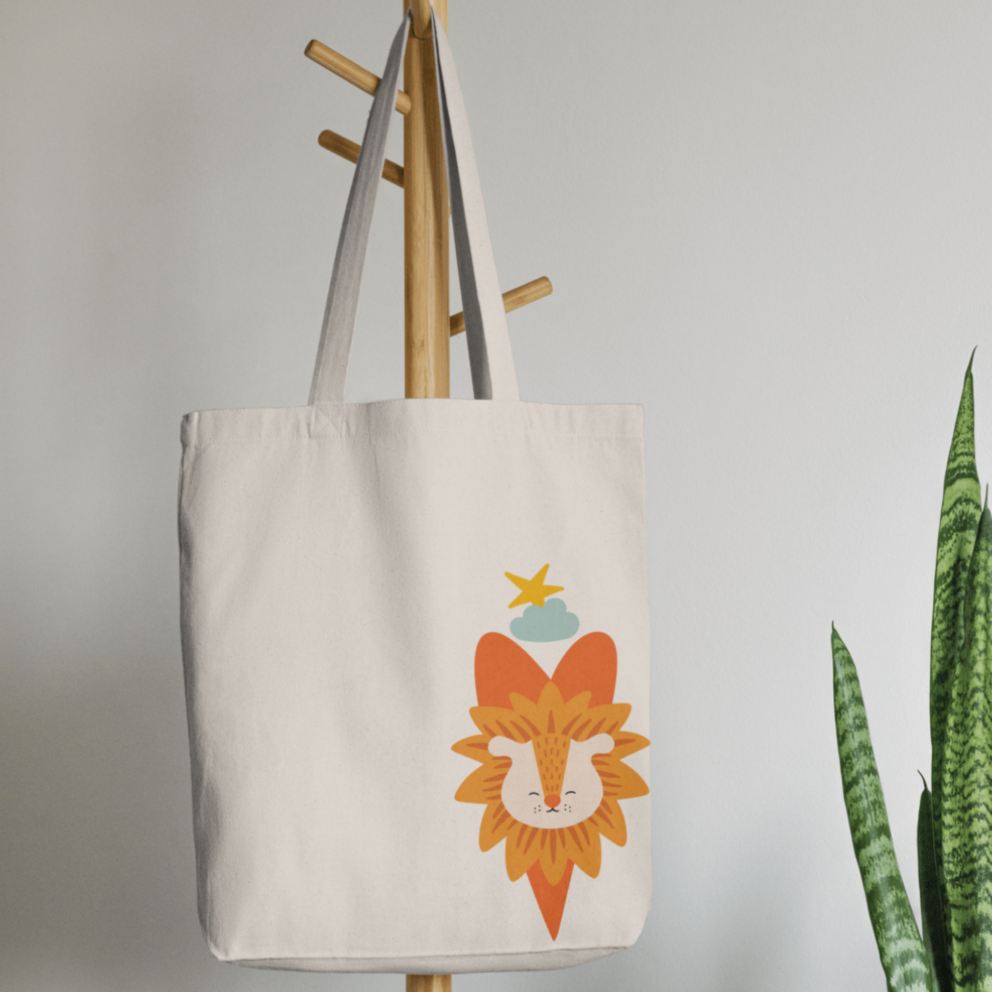 Bolsa Tote Bag color beige en  perchero, mostrando el diseño del león Sabino con un traje verde de la marca de ropa nube dentro de un corazón naranja. Arriba lo guía una estrella amarilla y una nube azul.