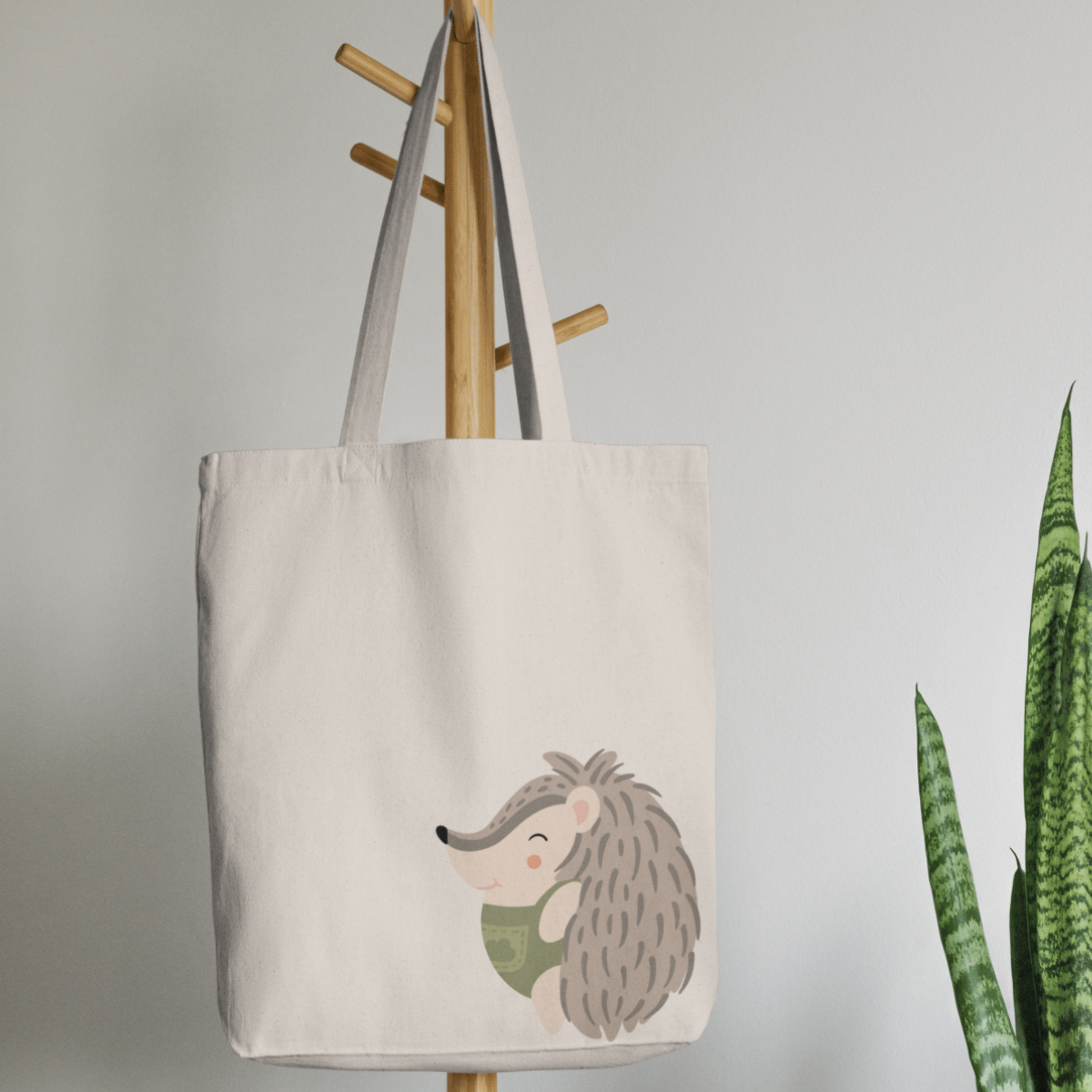 Bolsa Tote Bag color beige en  perchero, mostrando el estampado del puercoespin Filomeno con traje verde con dibujo de nube