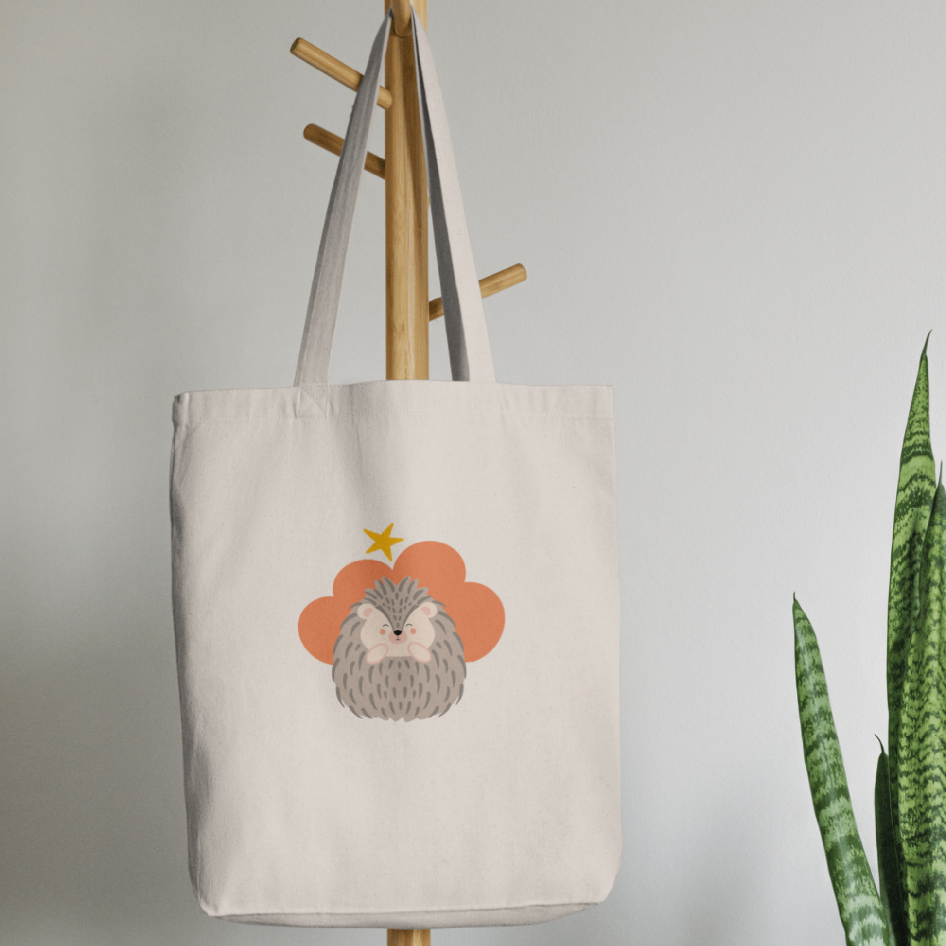 Bolsa Tote Bag color beige en  perchero, mostrando el estampado de puercoespín Filomeno en una Nube color naranja y una estrella amarilla