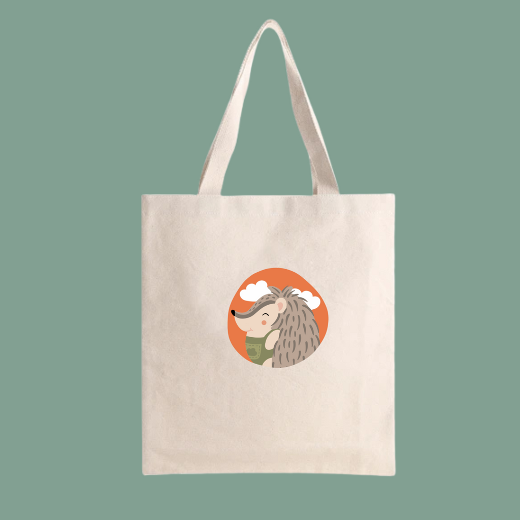 Bolsa Tote Bag color beige con estampado retrato del puercoespin Filomeno con un traje verde de la marca de ropa nube dentro de un círculo naranja con nubes.